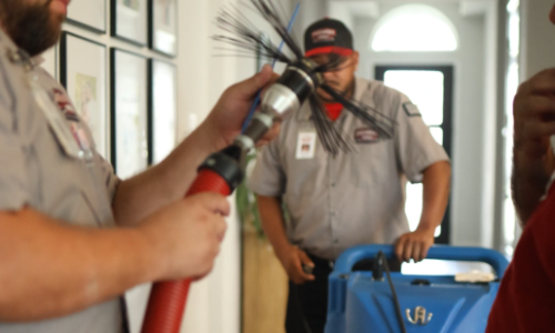 Rotating brush being inserted into an air duct opening to break up deep-seated dirt and debris.